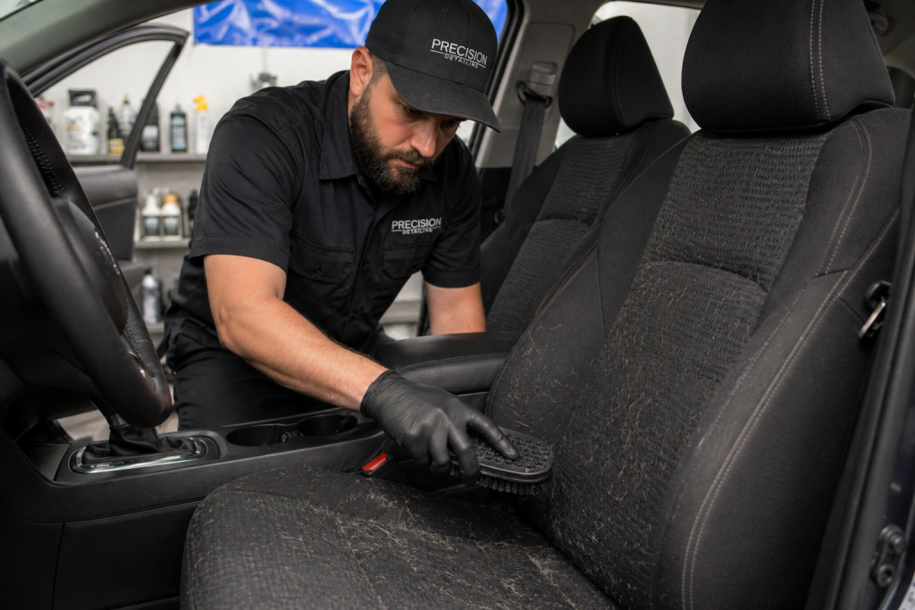Professional detailer using rubber brush for pet hair removal from car seats during agitation step